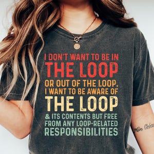 May include: Dark gray t-shirt with the text "I DON'T WANT TO BE IN THE LOOP" in red, "OR OUT OF THE LOOP. I WANT TO BE AWARE OF THE LOOP" in yellow, and "& ITS CONTENTS BUT FREE FROM ANY LOOP-RELATED RESPONSIBILITIES" in green.