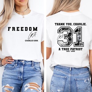 May include: White t-shirt with the word "FREEDOM" in bold black letters and a signature. The back of the shirt features the text "THANK YOU, CHARLIE." with the number "31" and the words "A TRUE PATRIOT 1993-2025".