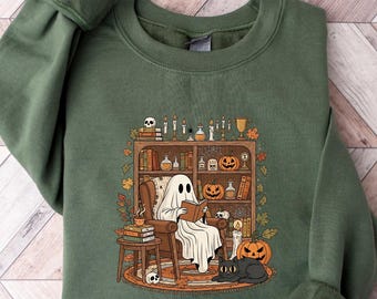 May include: Military green sweatshirt featuring a Halloween-themed graphic. The graphic depicts a ghost reading in a chair in front of a bookshelf with pumpkins, a black cat, and other spooky items. The text "MILITARY GREEN" is above the sweatshirt.