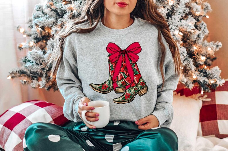 Pu&ograve; includere: Una felpa grigia con un design festivo di stivali da cowboy rossi con un fiocco rosso e accenti floreali verdi e rossi.