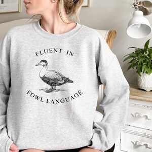 May include: Gray sweatshirt with a black and white illustration of a duck and the text "Fluent in Fowl Language".