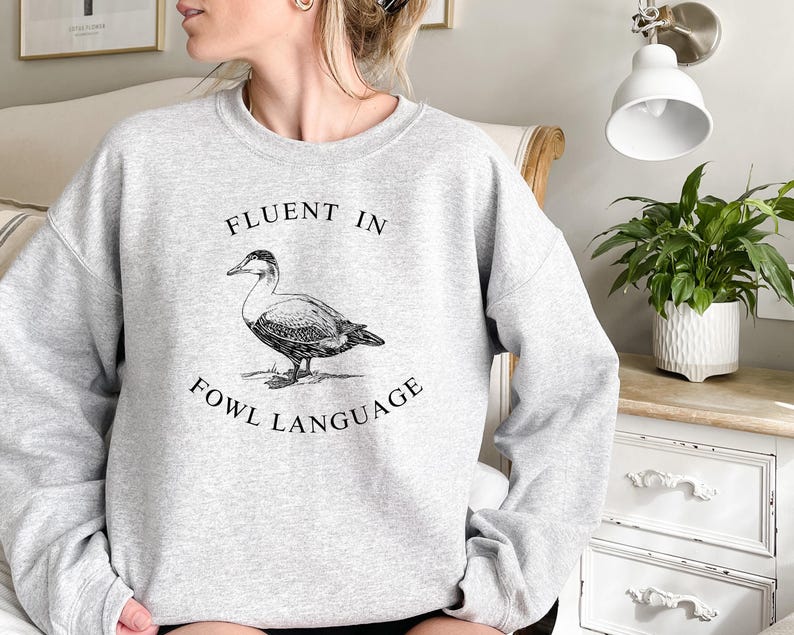 May include: Gray sweatshirt with a black and white illustration of a duck and the text "Fluent in Fowl Language".