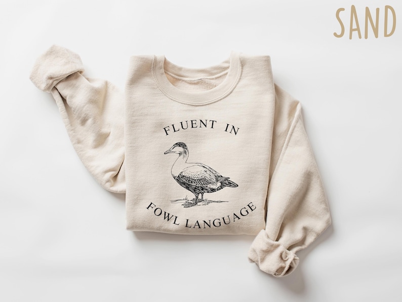 May include: A beige sweatshirt with the text "Fluent in Fowl Language" and a black and white illustration of a duck.