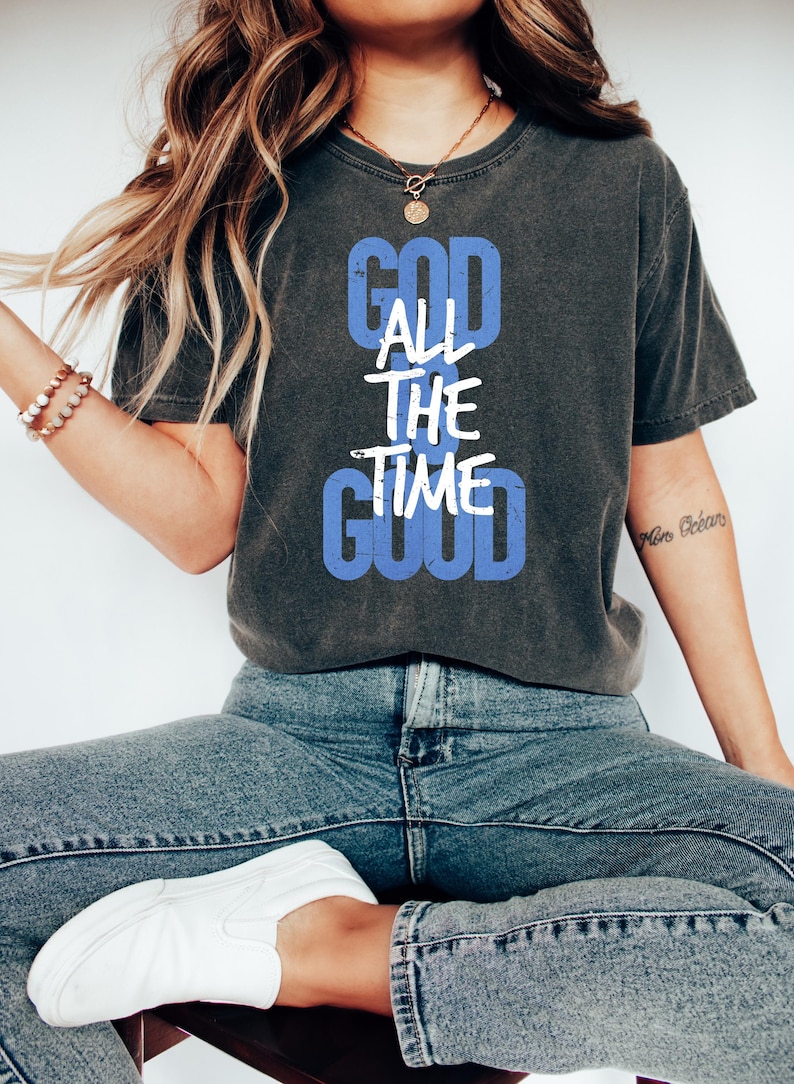 May include: A dark grey t-shirt with a white graphic that reads "God is good all the time" in a blue box.