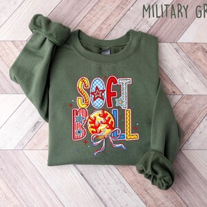 Puede incluir: Una sudadera verde con las palabras "Softball" en letras de colores y un gr&aacute;fico de una pelota de softbol.