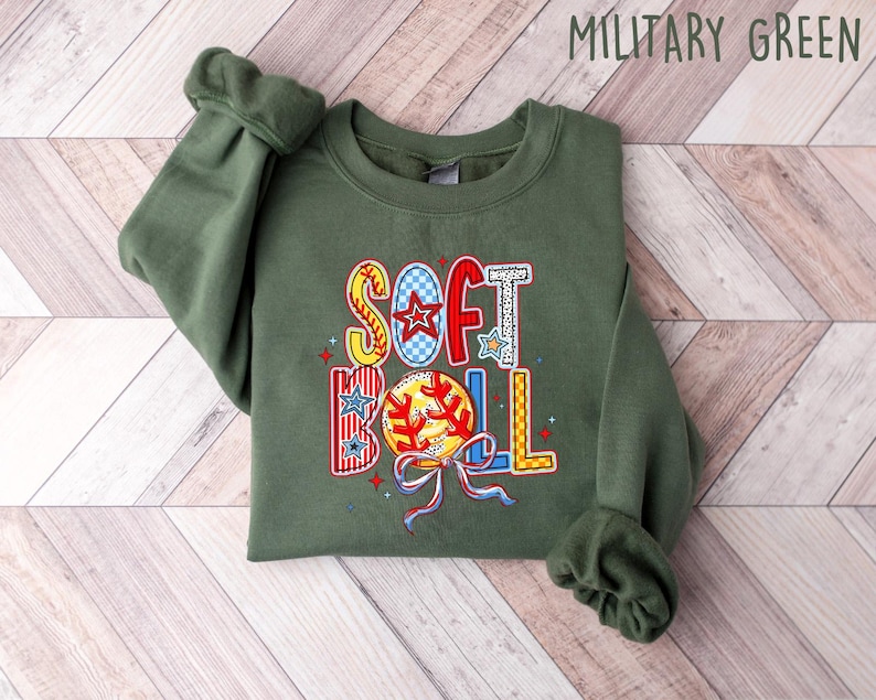 Puede incluir: Una sudadera verde con las palabras "Softball" en letras de colores y un gr&aacute;fico de una pelota de softbol.