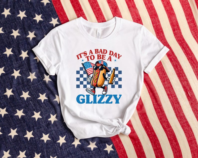 May include: White t-shirt with a cartoon hot dog wearing a red, white, and blue baseball cap and holding a beer. The text on the shirt reads "It's a bad day to be a Glizzy".