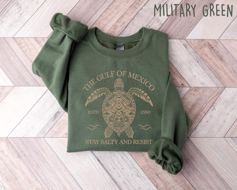 May include: A green sweatshirt with a gold graphic of a sea turtle with the text "The Gulf of Mexico" above it and "Stay Salty and Resist" below it. The text "Estd 1550" is also included on the graphic.