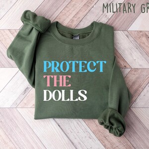 May include: A green sweatshirt with the text "PROTECT THE DOLLS" in blue, pink, and white lettering.