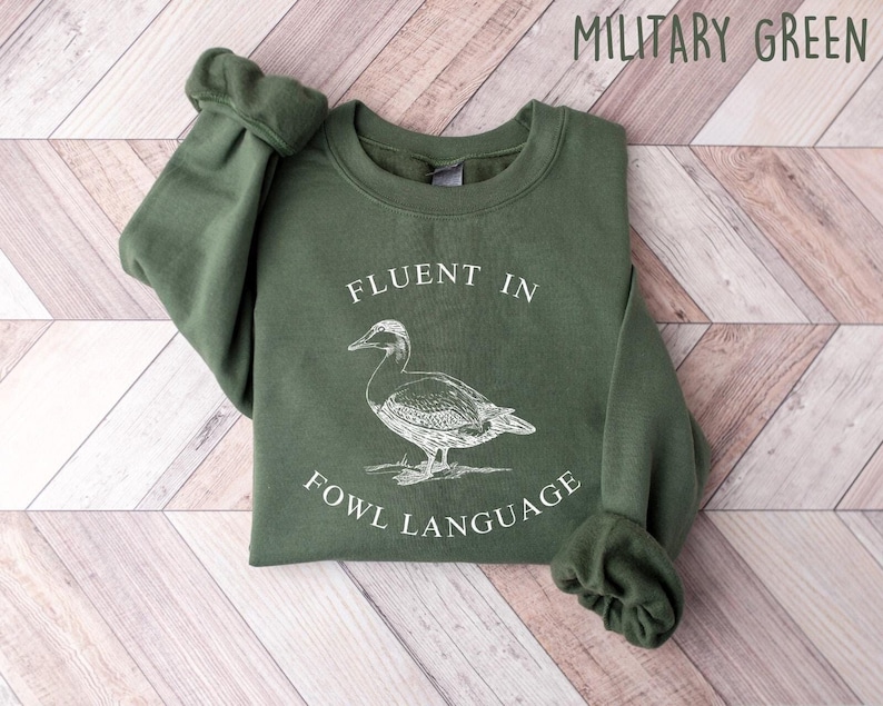 May include: A green sweatshirt with the text "Fluent in Fowl Language" and a drawing of a duck.