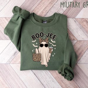 May include: Military green sweatshirt with a graphic of a ghost wearing sunglasses and a bow, holding a purse and a drink. The word "BOO-JEE" is above the ghost. Bats and stars are also in the design.