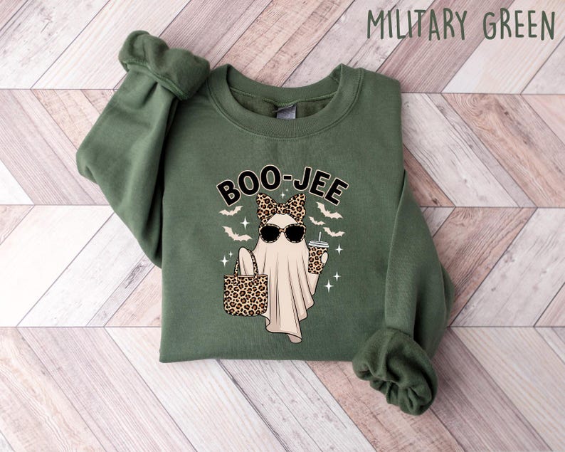 May include: Military green sweatshirt with a graphic of a ghost wearing sunglasses and a bow, holding a purse and a drink. The word "BOO-JEE" is above the ghost. Bats and stars are also in the design.
