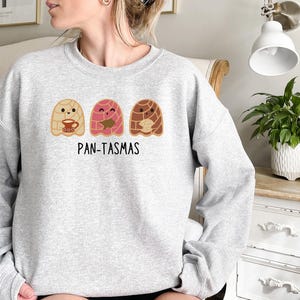 May include: A gray sweatshirt with a graphic of three cartoon pan dulce, or sweet bread, with the text "PAN-TASMAS" below.