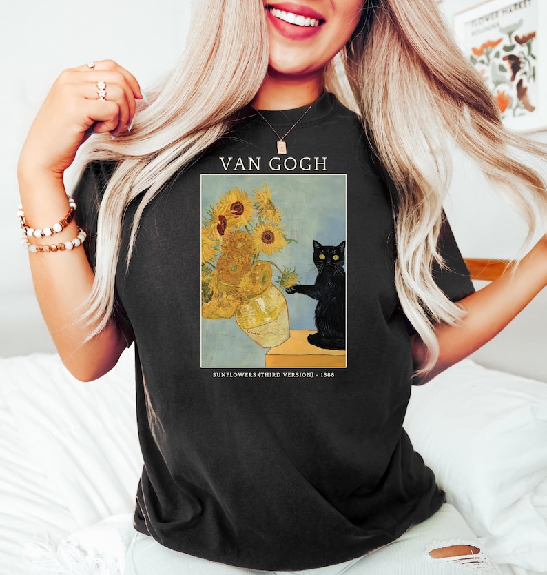May include: Black t-shirt featuring a print of Van Gogh's "Sunflowers (Third Version)" painting. The artwork includes a vase of sunflowers and a black cat. The text "VAN GOGH" and "SUNFLOWERS (THIRD VERSION) - 1888" are also printed on the shirt.