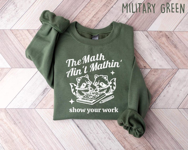 May include: A green sweatshirt with the text "The Math Ain't Mathin'" and a graphic of two raccoons using a calculator. The text "show your work" is below the graphic.