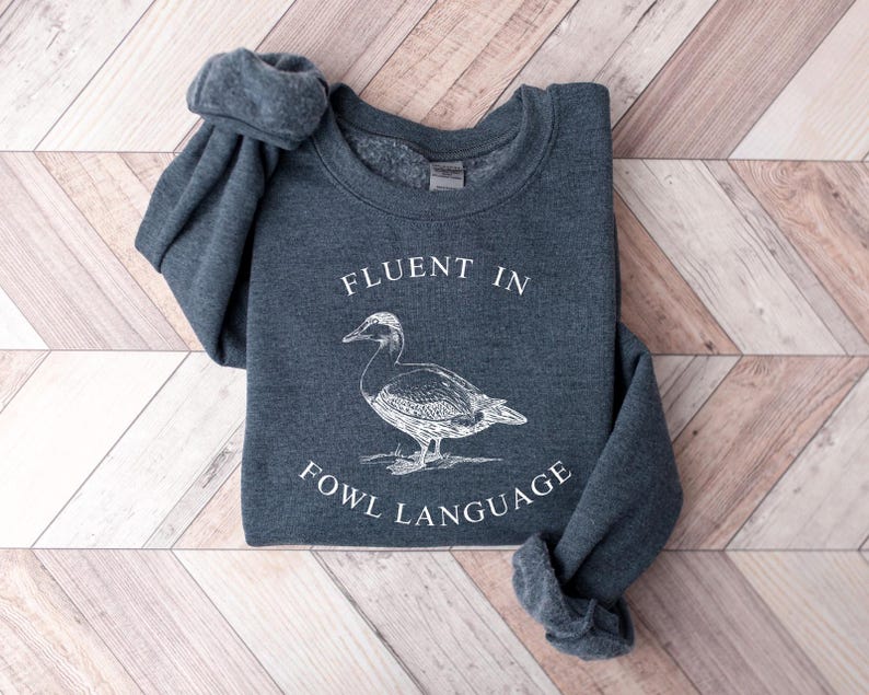 May include: A dark gray sweatshirt with the text "Fluent in Fowl Language" and a white illustration of a duck.