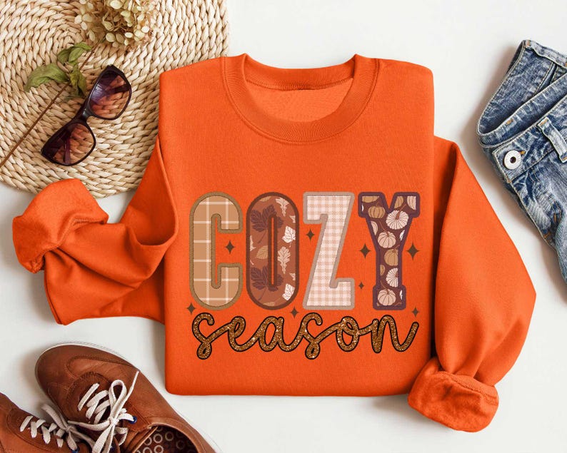 May include: Orange sweatshirt with the text "Cozy season" in brown, white, and orange letters with a plaid and floral pattern.
