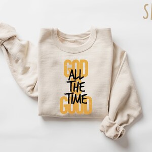 May include: A beige sweatshirt with the text "GOD ALL THE TIME GOOD" printed in black and yellow on the front.