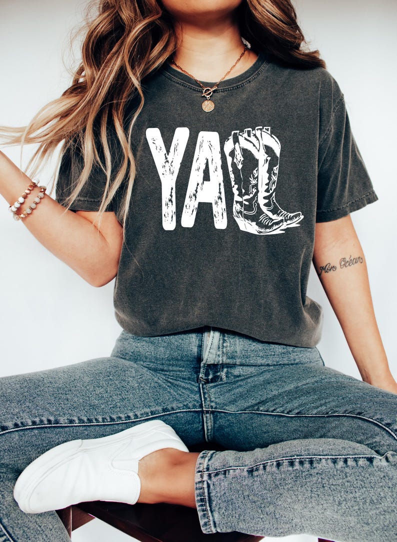 May include: A dark gray t-shirt with a white graphic of the word "Y'all" with a pair of cowboy boots.
