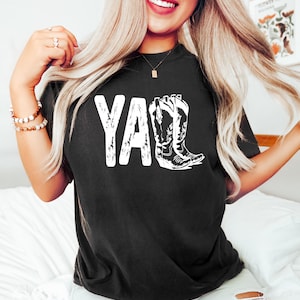 May include: Black t-shirt with a white graphic of the word "Y'all" and a pair of cowboy boots.