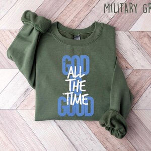 May include: A green sweatshirt with the text "God All The Time Good" in white and blue lettering.