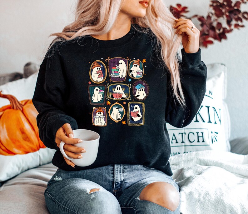 May include: Black sweatshirt featuring a grid of nine framed ghost illustrations. Each ghost is depicted reading books, wearing hats, or holding books. The frames have a gold border. The sweatshirt is a casual, comfortable style.