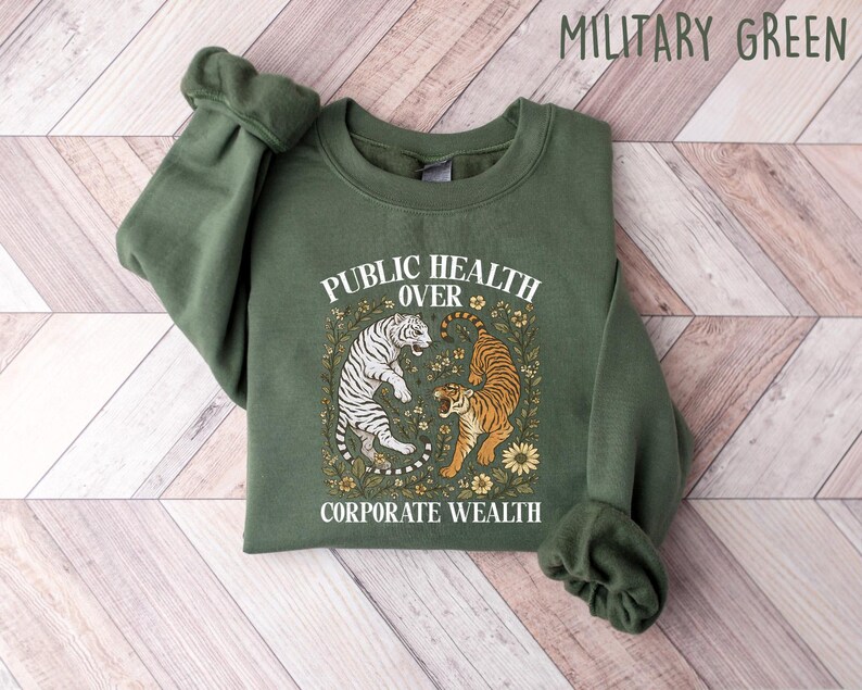 Puede incluir: Sudadera verde militar con el texto "PUBLIC HEALTH OVER CORPORATE WEALTH". El dise&ntilde;o presenta dos tigres rodeados de elementos florales. La sudadera est&aacute; hecha de un material suave.