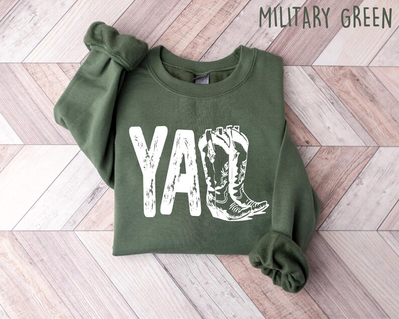 May include: A green sweatshirt with the word "Y'all" printed in white with a distressed look. The word is accompanied by a graphic of two white cowboy boots.
