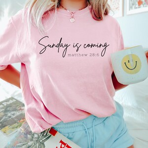 May include: A pink t-shirt with the text "Sunday is coming Matthew 28:6" printed on the front.