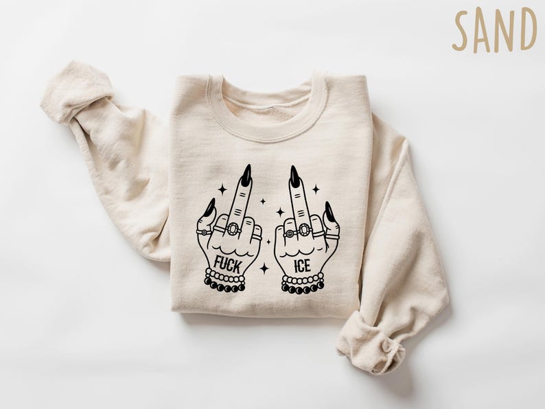 May include: Sand-colored sweatshirt with a black graphic of two hands giving the middle finger. The hands are adorned with rings, bracelets, and long black fingernails. The words "FUCK" and "ICE" are printed below the hands.
