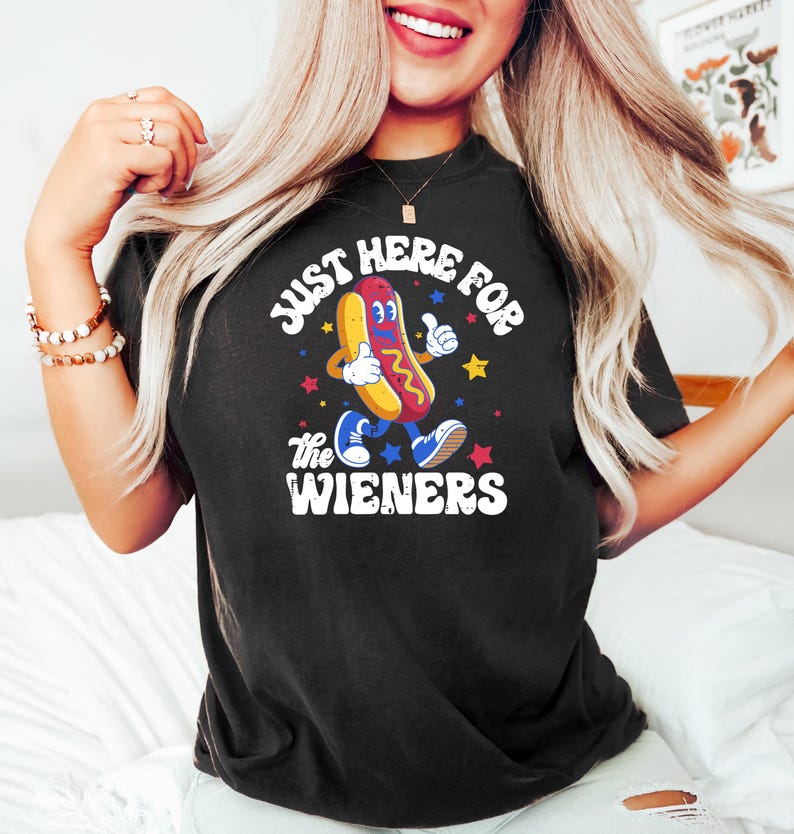 May include: Black t-shirt with the text "JUST HERE FOR THE WIENERS" and a cartoon hot dog character giving a thumbs up. The hot dog is wearing blue shoes and is surrounded by stars.
