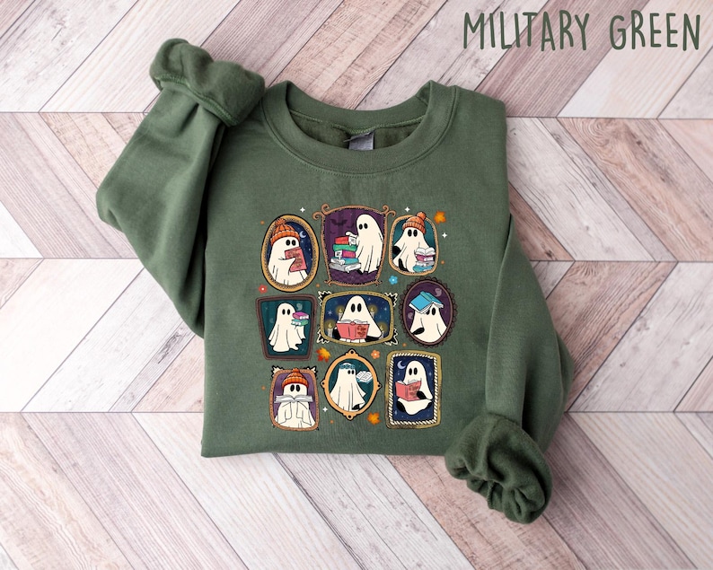 May include: Military green sweatshirt featuring a framed graphic of cartoon ghosts reading books. The ghosts are wearing hats and scarves. The sweatshirt is made of a soft material.