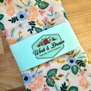 May include: A set of white cotton napkins with a floral pattern in shades of blue, pink, and yellow. The napkins are packaged with a blue and white label that reads "Work & Dream Everyday Cotton Napkins".