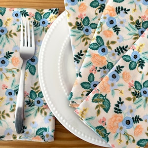 May include: Three floral patterned napkins in shades of blue, green, peach, and yellow on a white plate with a silver fork.