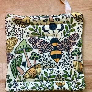 Puede incluir: Un agarrador de olla acolchado verde, amarillo y marr&oacute;n con una abeja, setas y dise&ntilde;os florales.