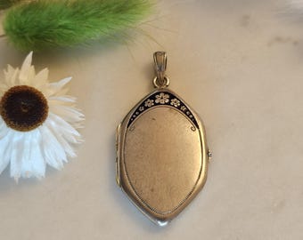 May include: Silver locket pendant with a floral design around the edge. The locket is oval shaped and has a smooth surface.