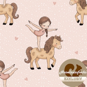 Op de afbeelding: Een herhalend patroon met cartoon illustraties van lichtbruine paarden en meisjes in roze turnpakjes. De meisjes balanceren op de paarden, met uitgestrekte armen. De achtergrond is lichtroze met kleine witte stippen en roze hartjes.