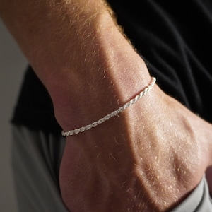 May include: A silver rope chain bracelet on a person's wrist.