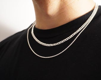 May include: Two silver chains, one a curb chain and the other a rope chain, layered on a person's neck.