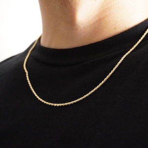 May include: A gold rope chain necklace on a person wearing a black shirt.
