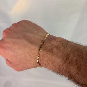 Puede incluir: Una pulsera de cadena de eslabones dorada. La pulsera está hecha de pequeños eslabones entrelazados y se lleva en la muñeca. La pulsera tiene un diseño sencillo y clásico.