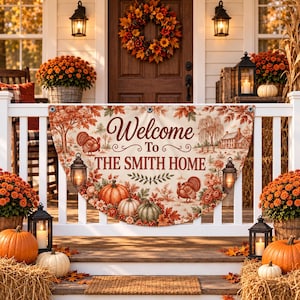Op de afbeelding: Een halfronde stoffen banner met een herfstprint van pompoenen, kalkoenen, lantaarns en herfstbladeren. De tekst luidt Welcome To THE SMITH HOME. De banner is bevestigd aan een witte veranda-leuning met metalen ringen.