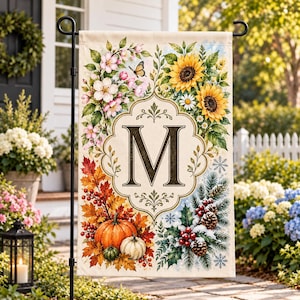 May include: A rectangular garden flag featuring a central ornate frame with the letter M. The design displays four seasonal quadrants: spring flowers with a butterfly, summer sunflowers, autumn pumpkins with fall leaves, and winter pine with snow.