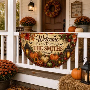 以下が含まれることがあります： Welcome To THE SMITHSという文字が書かれた半円形の装飾看板。オレンジ色のカボチャ、ヒマワリ、秋の葉、クモの巣、コウモリ、2つのランタンのイラストが、明るい色のテクスチャ背景に描かれています。