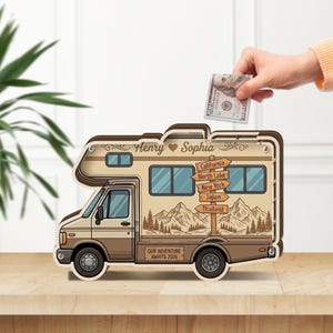 Op de afbeelding: Een houten spaarpot in de vorm van een camper met de namen Henry en Sophia, een wegwijzer met locaties zoals California, North Lake, New York, Japan en Thailand, en de tekst Our Adventure Awaits 2026 op de zijkant gedrukt.