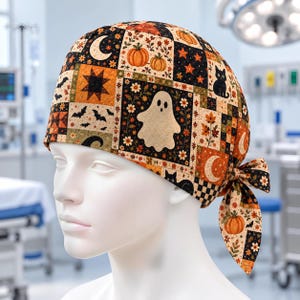 May include: A scrub cap featuring a patchwork pattern of Halloween-themed illustrations including ghosts, black cats, orange pumpkins, crescent moons, stars, bats, and autumn leaves on a black background, tied with a fabric bow at the back.