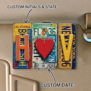 Può includere: Un'opera d'arte personalizzata con targhe automobilistiche, con iniziali e una data personalizzata. Il design incorpora targhe della California, Florida e New York, con un cuore rosso e la data 02-14-2026. Il testo "CUSTOM INITIALS & STATE" e "CUSTOM DATE" è visibile.