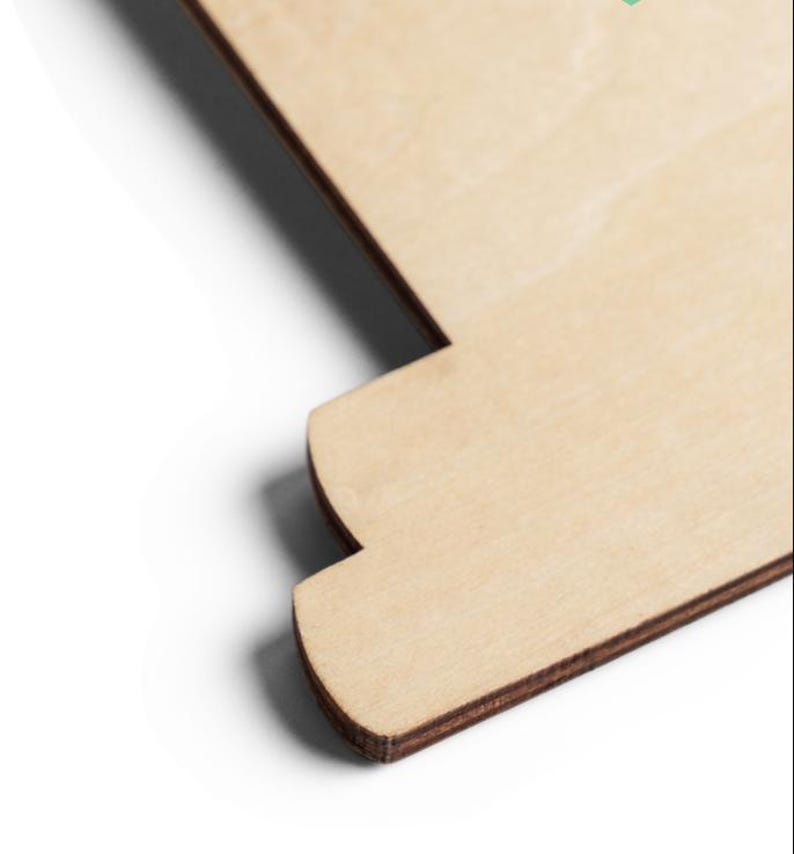 Puede incluir: Un recorte de madera plano y de color claro con una superficie de grano natural y suave. El objeto presenta un perfil de borde escalonado distintivo con una secci&oacute;n de esquina curva, mostrando la textura estratificada del contrachapado en los bordes oscuros.