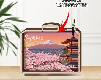 Peut inclure: Un objet décoratif en forme de valise en bois représentant un paysage japonais avec le Mont Fuji, des fleurs de cerisier et une pagode. Le texte "Sophia's Travel Fund To Japan" est visible. Les mots "CUSTOM LANDSCAPES" sont également affichés.