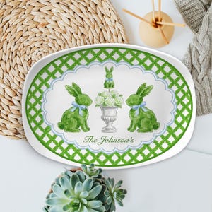 May include: An oval serving platter with a green lattice border and a white center. The center features green bunnies with blue bows, a floral arrangement, and the text "The Johnson's". The platter is perfect for Easter.